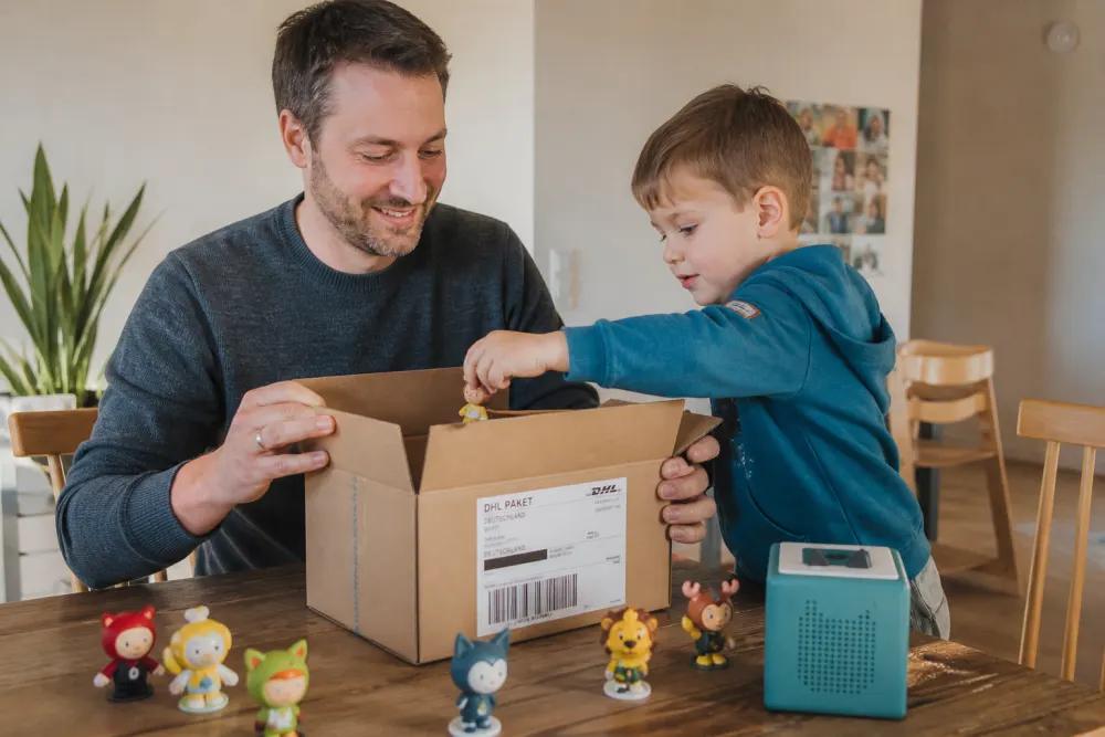 Vater und Sohn packen Tonie-Figuren für den kostenlosen DHL-Versand ein